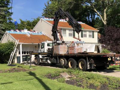 Local roofing crew tearing off old shingles while a boom truck delivers new shingle bundles to the roof