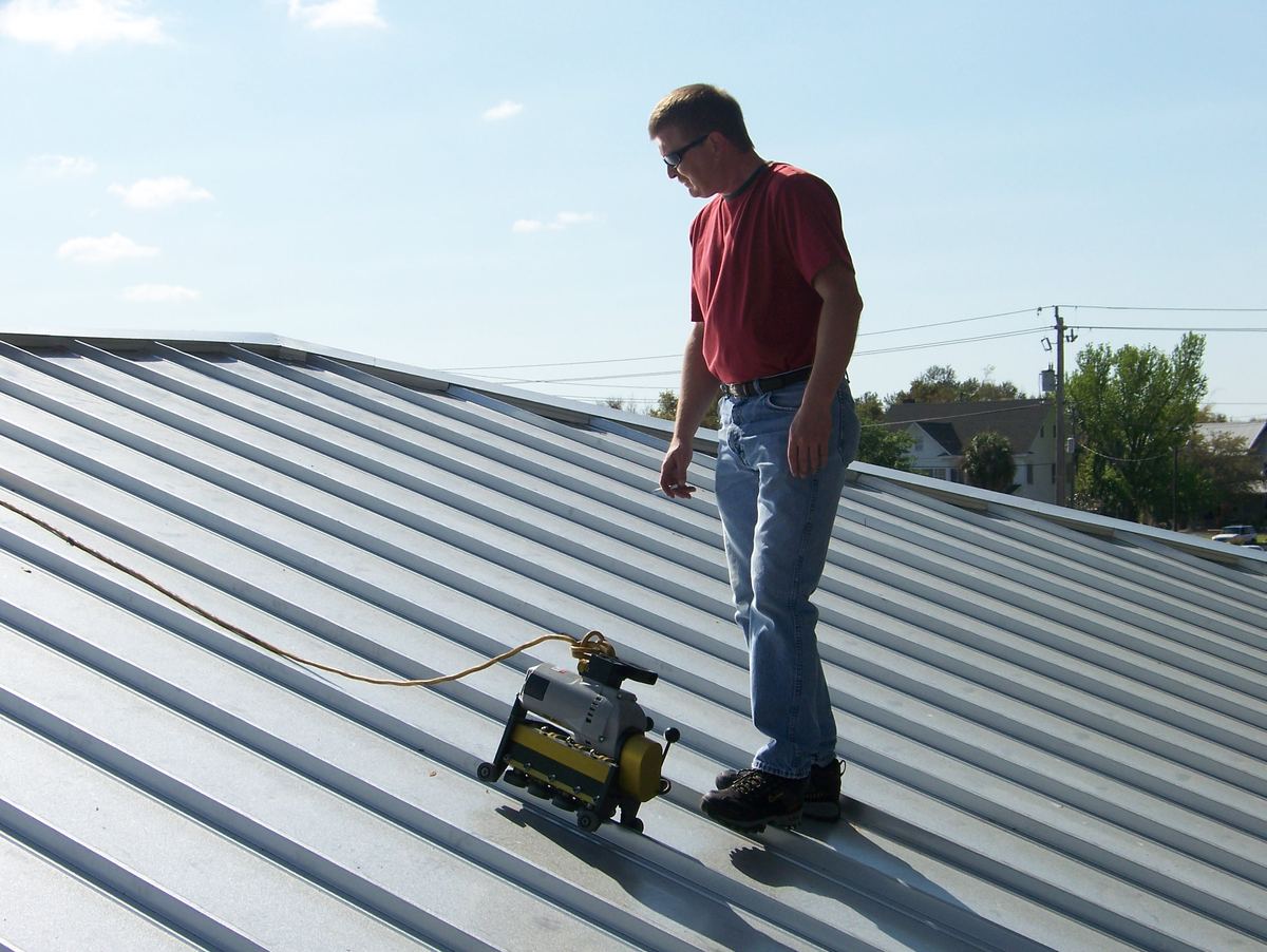 Roofer operating a seaming machine to join standing-seam metal roof panels
