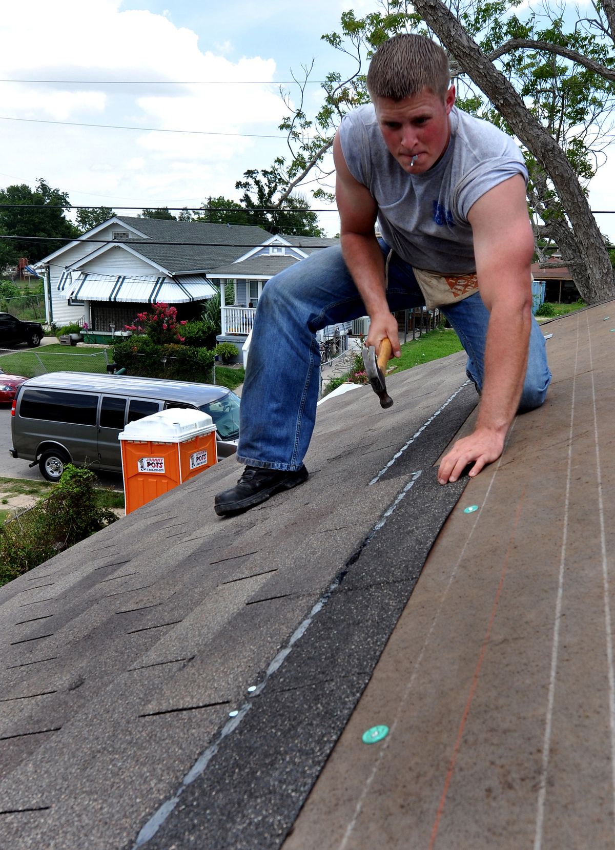 Roofer nailing new asphalt shingles into place on a residential roof